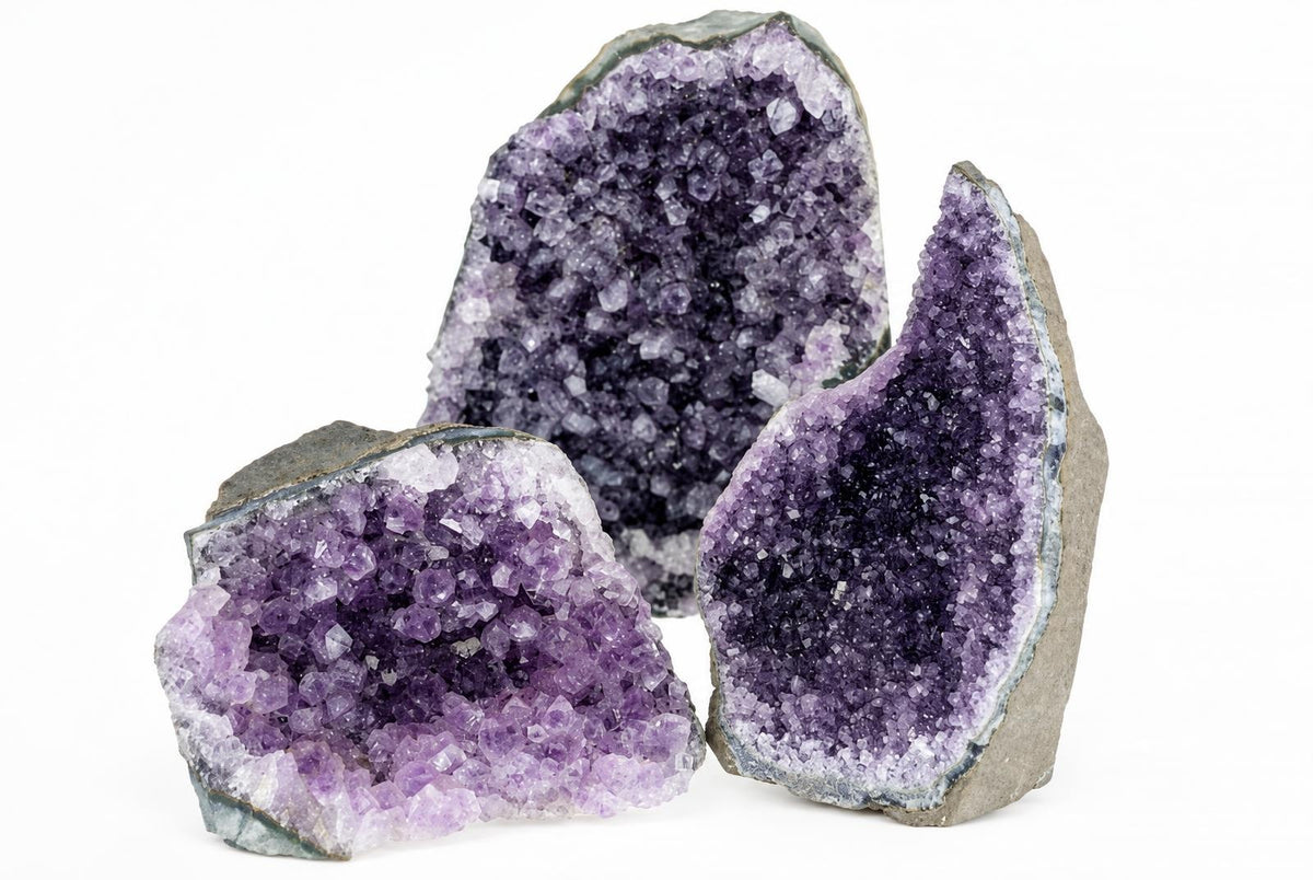 Three amethyst geode slices with purple crystals on a white surface.