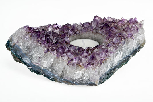 Amethyst candlelight – A: An amethyst geode slice with purple and clear crystals, a central white candle, on a pale surface.