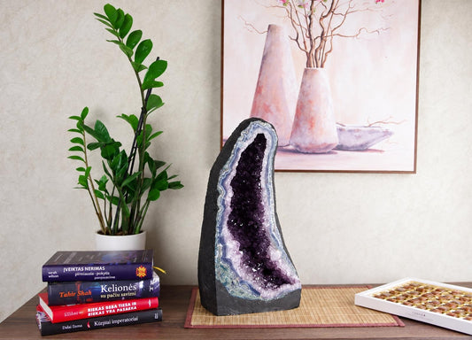 A large amethyst geode with dark outer rock and purple crystals sits on a wooden surface.