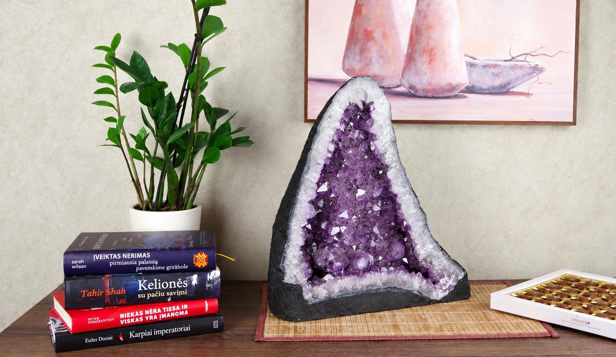 A large amethyst geode with purple crystals inside, set on a dark base and placed on a wooden surface.