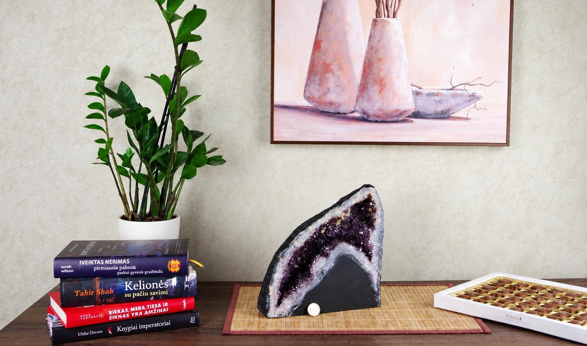 A large amethyst geode slice with purple crystals and a dark outer rind stands on a bamboo mat.