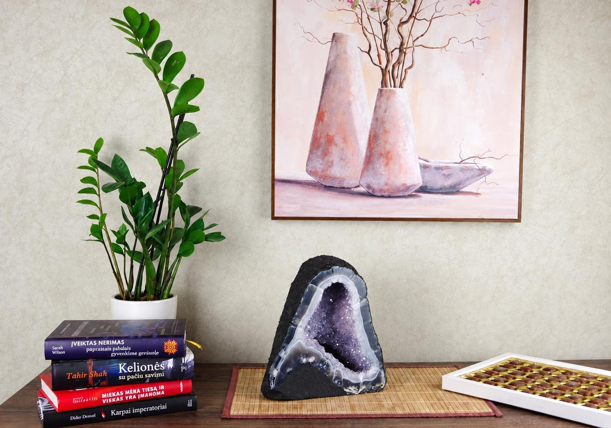 A large amethyst geode slice with a dark exterior and purple crystal interior sits on a bamboo mat.