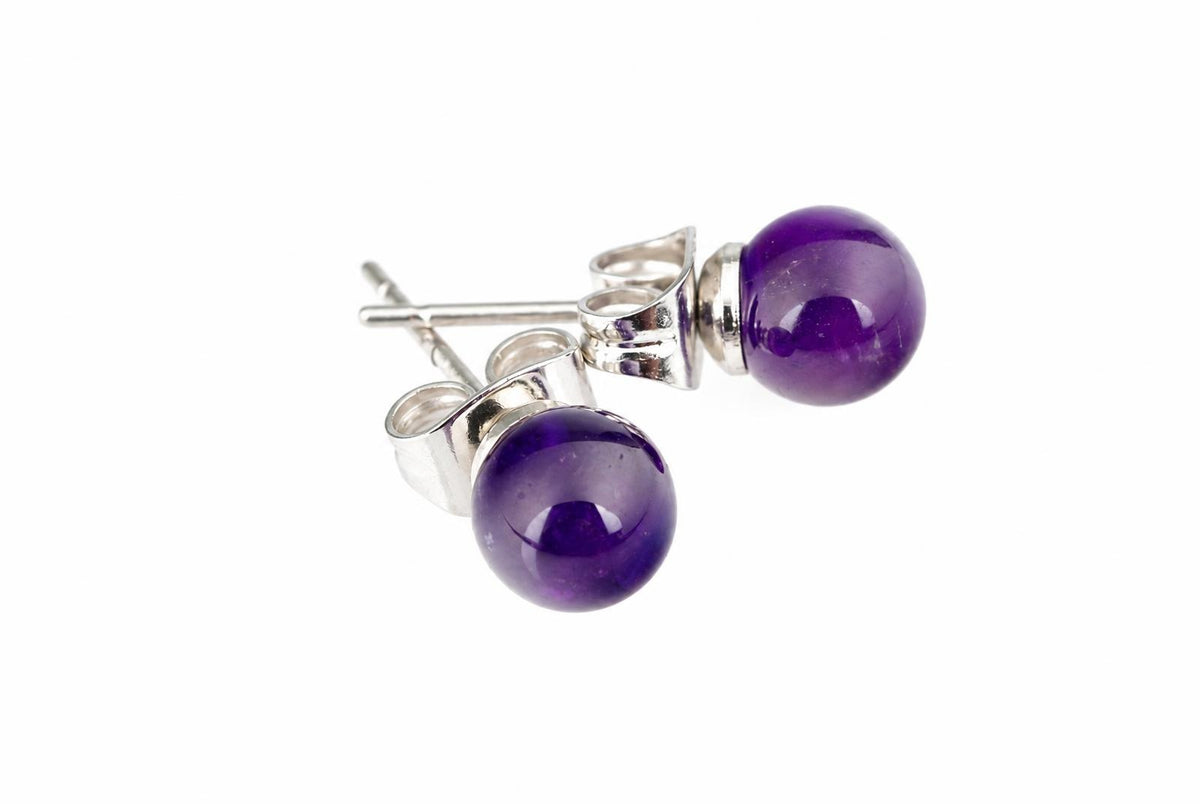 A pair of silver-toned stud earrings with round dark purple amethyst stones on a white surface.
