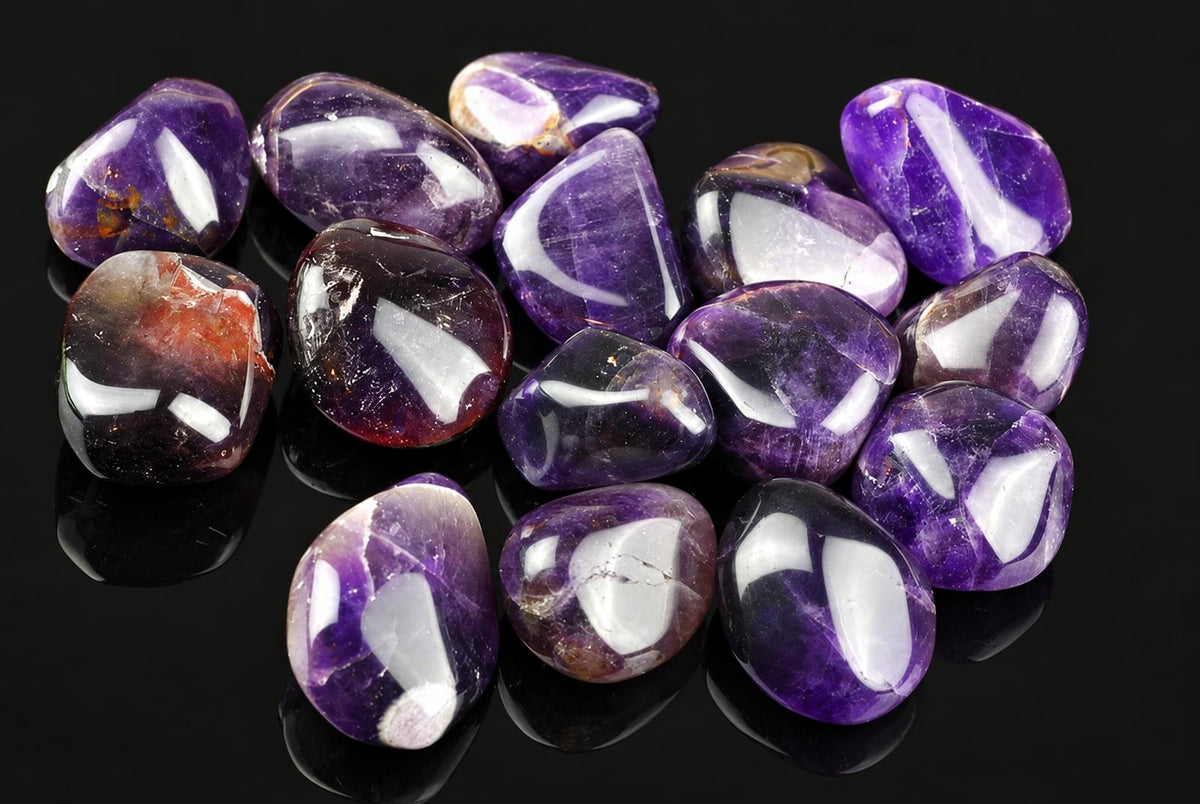A pile of polished amethyst tumbled stones in purple and white on a dark surface.