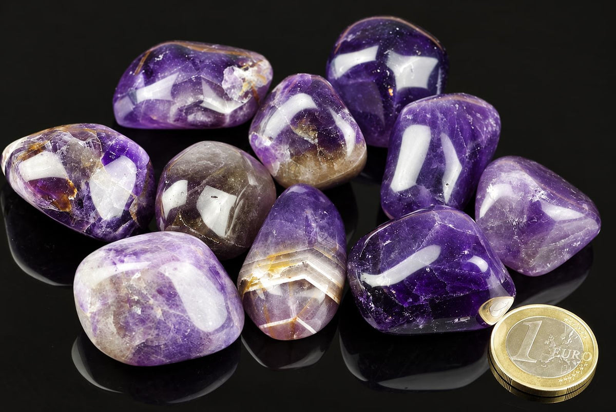 A group of polished amethyst stones in purple and white, arranged on a dark surface with a one-euro coin for scale.