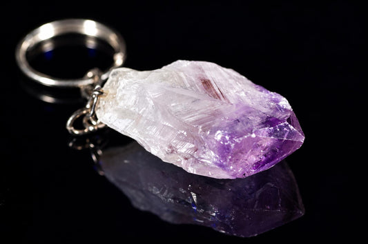 A silver-toned keychain with a rough, translucent crystal pendant that is white and purple on a dark surface.