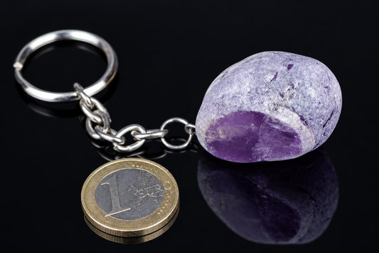 A silver-toned keychain with a chain, ring and a round purple stone on a dark reflective surface.