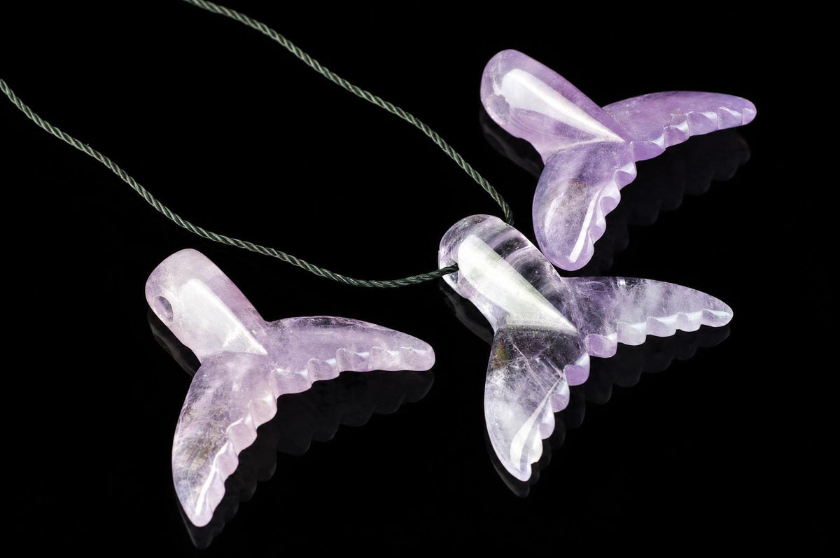 Three translucent purple dolphin-tail pendants on a dark surface, each with scalloped edges and a green cord.