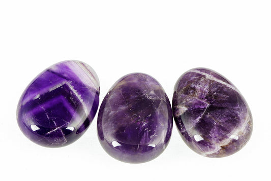 Three polished amethyst stones with deep purple and white banding, arranged horizontally on a pale surface.
