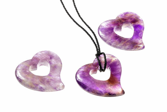 Three polished heart-shaped pendants with purple and white swirls, one on a black cord against a white background.