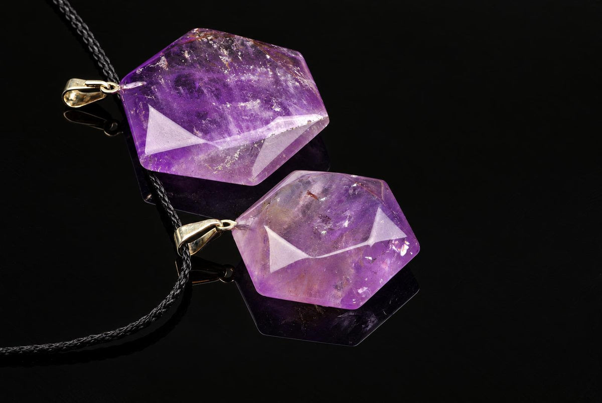 Purple hexagonal amethyst pendants with faceted edges and metal loops are arranged with black cords on a glossy dark surface.