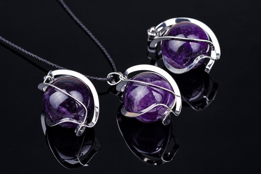 Three silver-toned pendants with round purple spheres on dark cords, arranged diagonally on a reflective black surface.