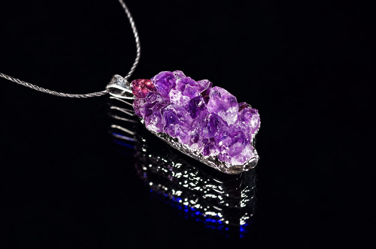 A silver-toned pendant with a cluster of purple amethyst crystals on a dark reflective surface.