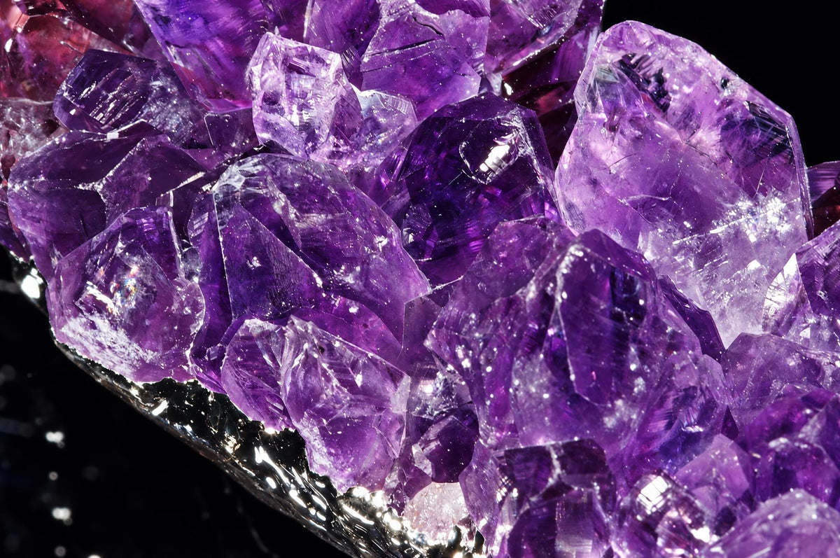 A cluster of purple amethyst crystals with varying shades and facets, resting on a dark surface.