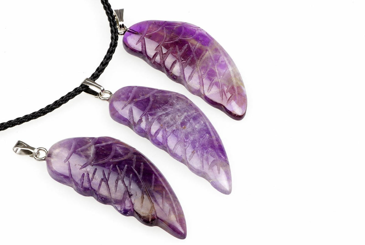 Three purple amethyst pendants shaped like wings, each with carved vein details and a silver-toned bail on a black cord against a white background.