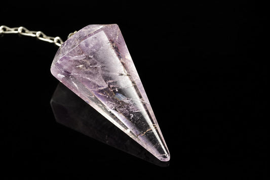 A silver-toned chain holds a faceted, purple and clear crystal pendulum on a dark surface.