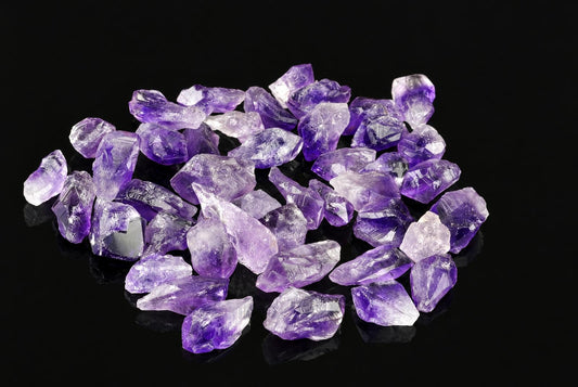 A pile of rough, purple and clear amethyst crystals on a dark surface.