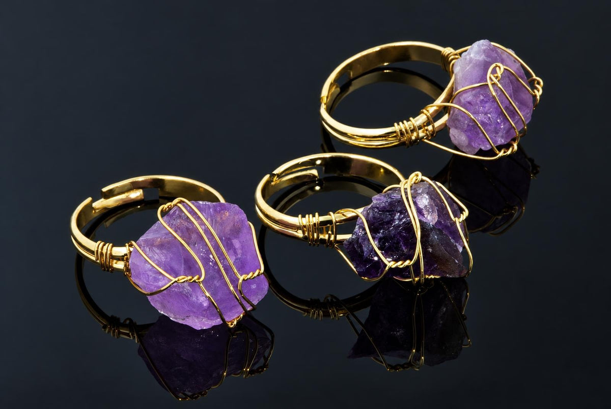 Gold-coloured rings hold rough purple crystals wrapped in thin wire on a dark reflective surface.