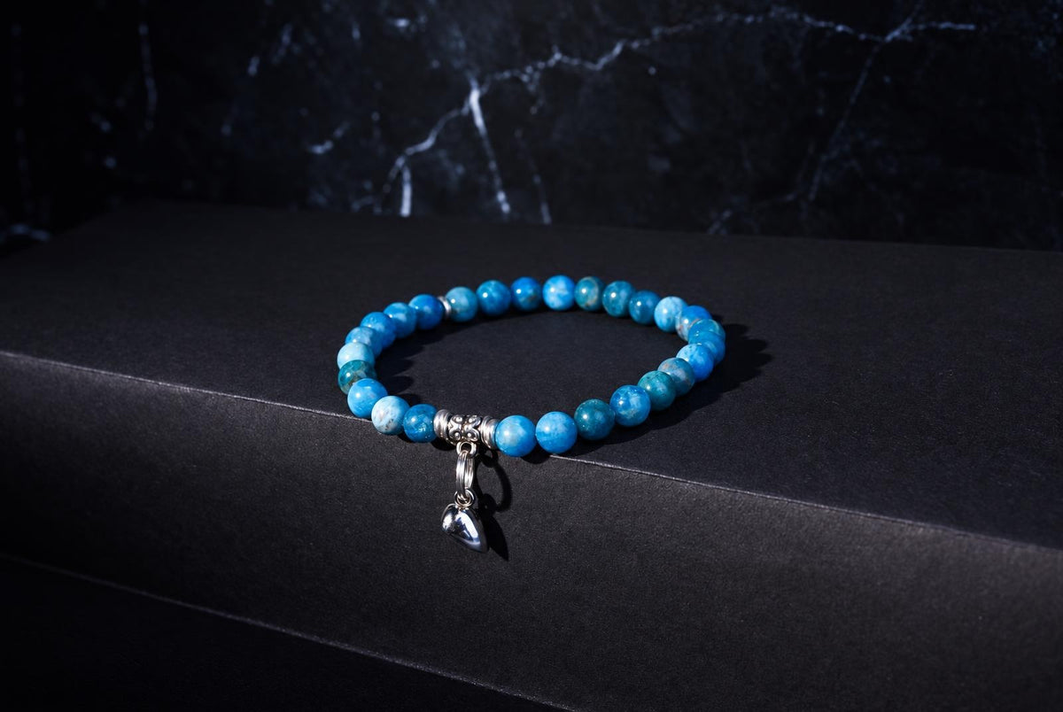 A bracelet with round blue beads and a silver heart charm rests on a dark surface.