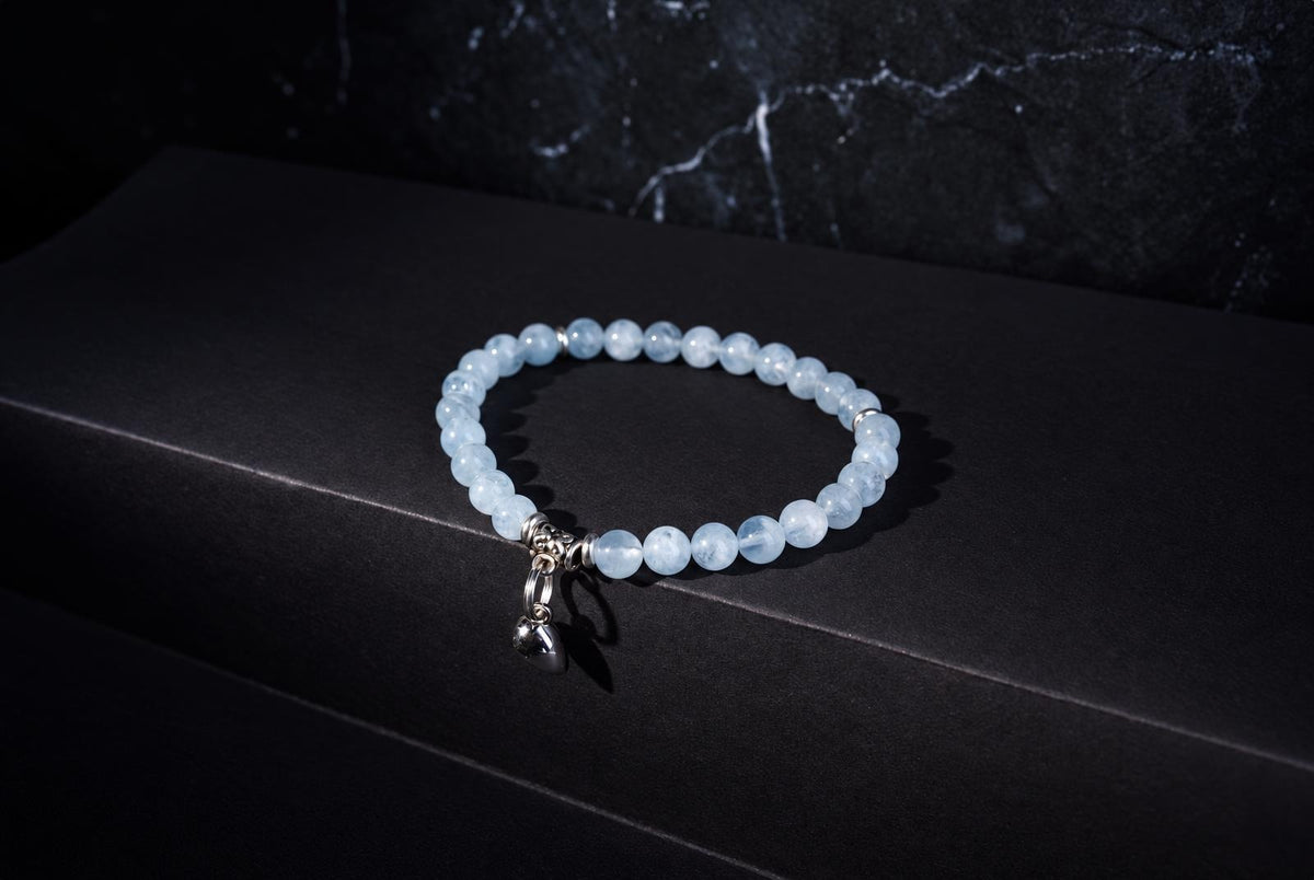 A bracelet with pale blue beads and a silver heart charm rests on a dark surface.