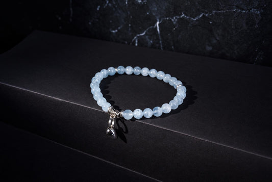 A bracelet with pale blue beads and a silver heart charm rests on a dark surface.