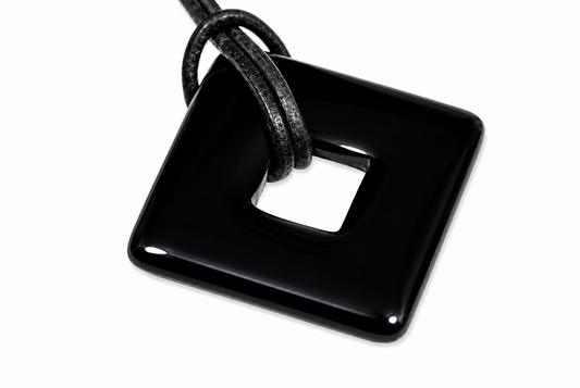 A glossy black square pendant with a central hole, threaded by a textured black cord against a white background.