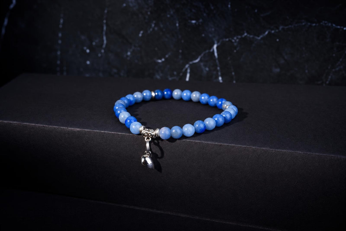 Blue quartz bead bracelet with silver heart charm on dark surface.