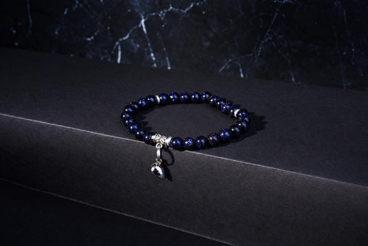 Bracelet with sparkling dark blue round beads, ornate silver spacers and a hanging heart charm against a dark background.