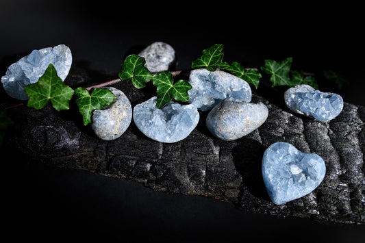 Pale blue crystal-filled stones rest on a dark textured surface among green leaves.