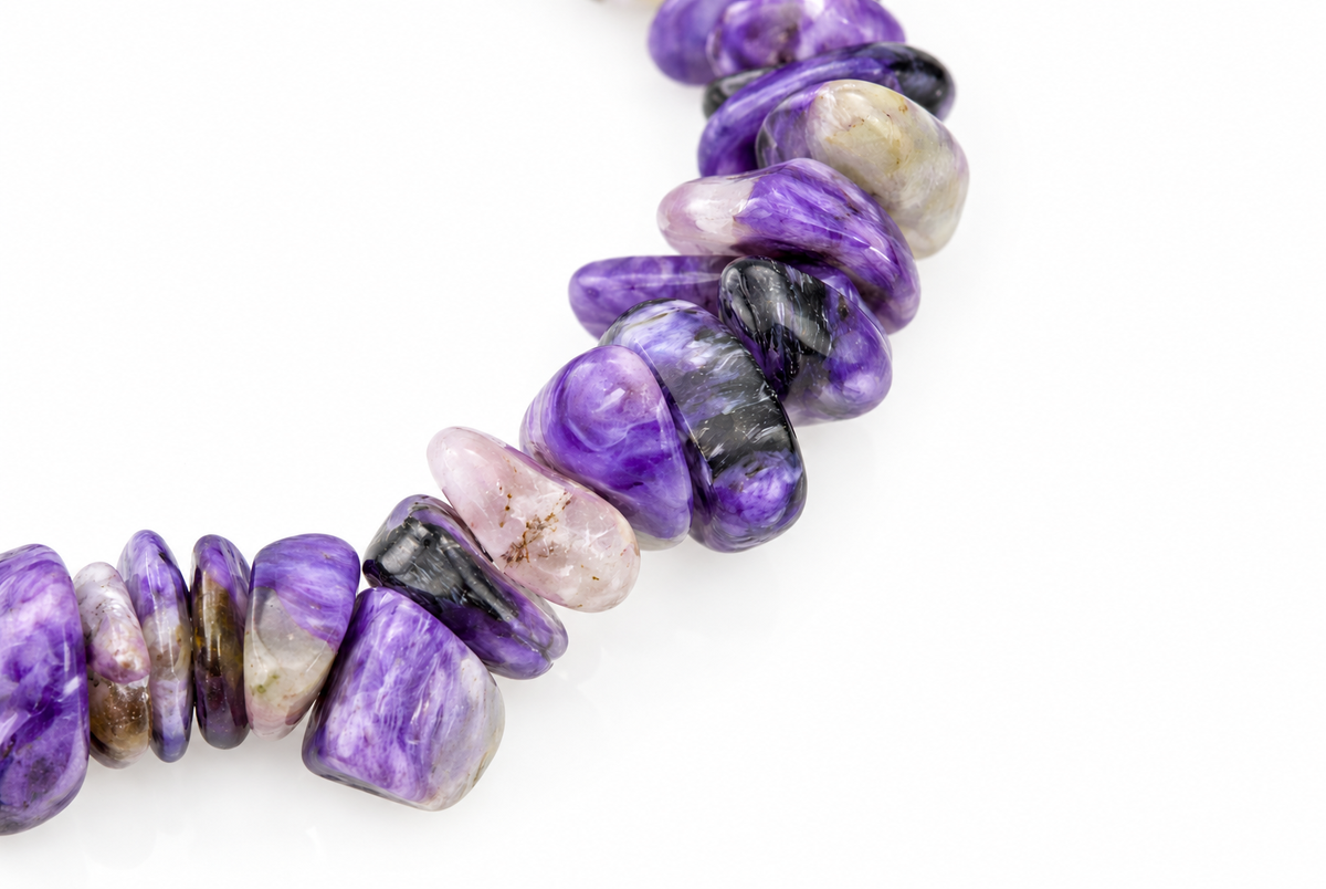 A strand of polished, irregular chips in purple, black, and pale tones arranged on a white surface.