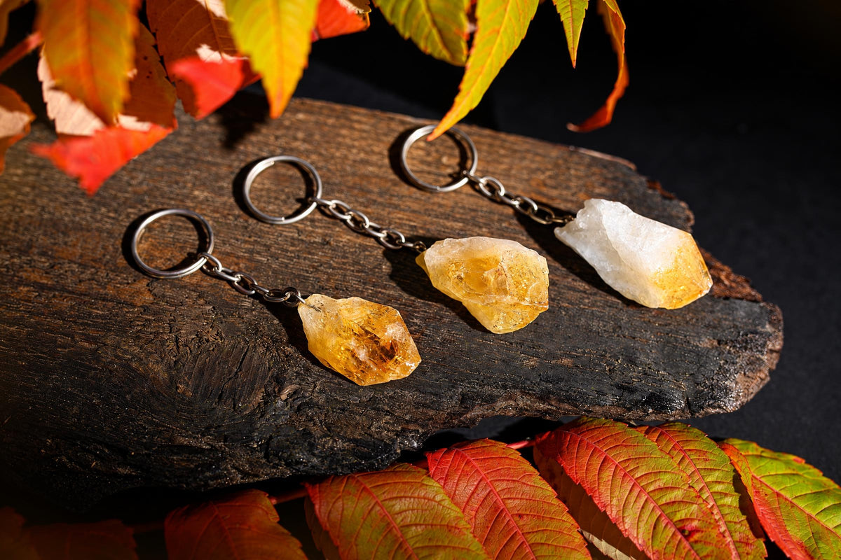 Keychains with rough yellow crystal points and silver-tone chains rest on a wooden surface among red-orange leaves.