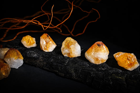 Yellow-orange crystal points with rough white bases rest on a dark textured surface beneath thin brown branches.