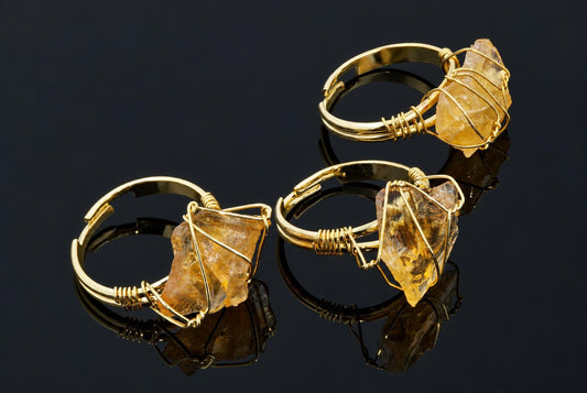 Gold-coloured rings hold rough yellow crystals wrapped in thin wire on a dark reflective surface.