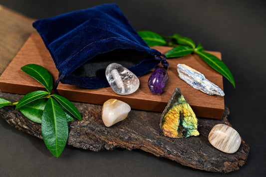 A dark blue pouch and clear, purple, pale and iridescent stones arranged on wood with green leaves.