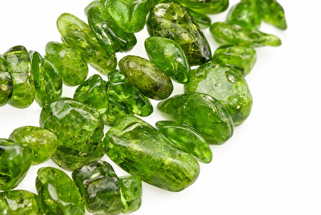 A pile of polished, translucent green diopside chips on a white surface.