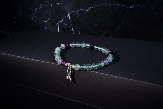 Fluorite bracelet with translucent green and purple round beads, ornate silver spacers and a hanging heart charm on a dark background.