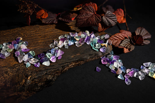 Small translucent purple, green and clear stones rest on a wooden surface beside reddish leaves.