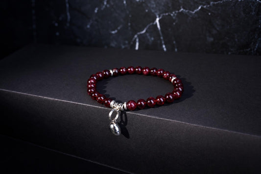 A bracelet with round red beads and a silver heart charm rests on a dark surface.