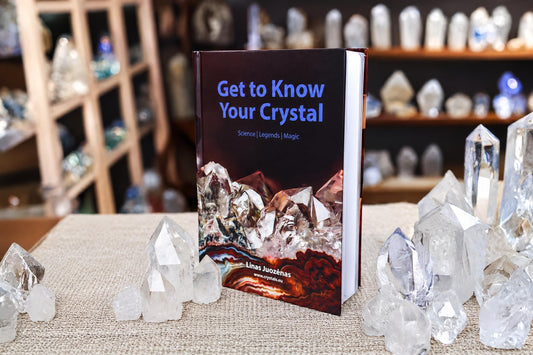 The Get to Know Your Crystal book stands among clear crystal points on a woven surface, with blurred shelves in the background.