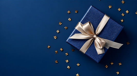 A blue gift box tied with a pale bow lies on a dark blue background scattered with small gold-coloured decorations.