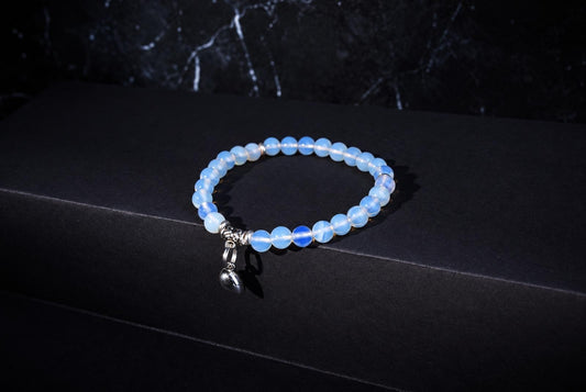 Glass opal bracelet with translucent pale blue round beads, ornate silver spacers and a hanging heart charm on a dark background.