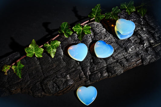 Smooth blue-white heart-shaped pieces rest on a dark textured surface beside green leaves.