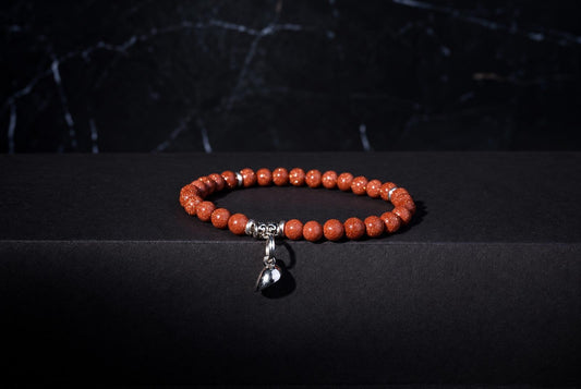 Goldstone bracelet with sparkling reddish-brown round beads, ornate silver spacers and a hanging heart charm against a dark background.