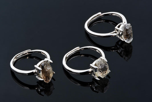 Silver-tone rings hold clear crystals with dark inclusions on a dark reflective surface.