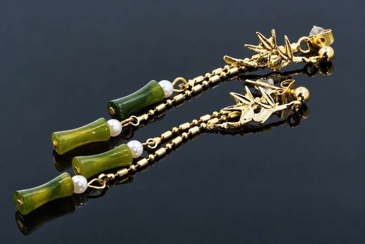 A pair of gold-toned stud earrings with starfish tops, green bamboo-style beads and white pearls on a dark reflective surface.
