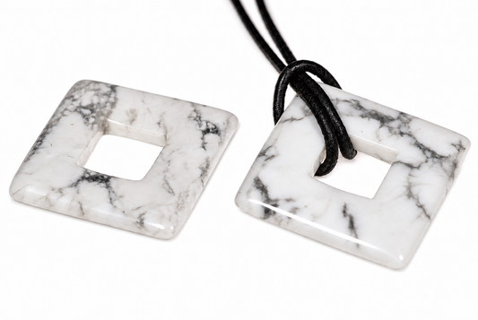 Two square, white and grey veined stone pendants with a central hole; one has a black cord threaded through it.
