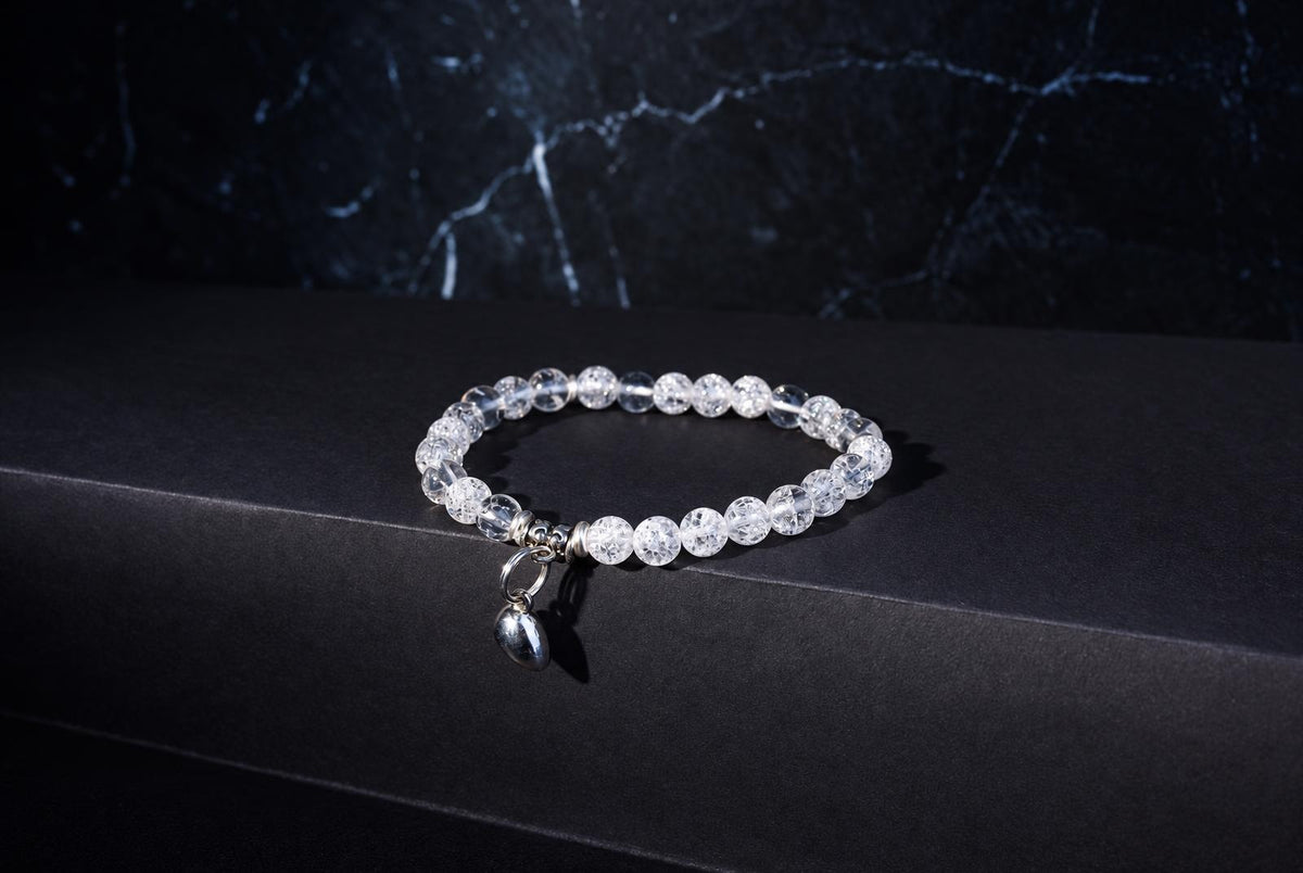 A bracelet with clear, crackled beads and a silver charm rests on a dark surface.