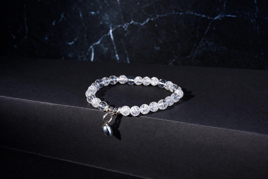A bracelet with clear, crackled beads and a silver charm rests on a dark surface.