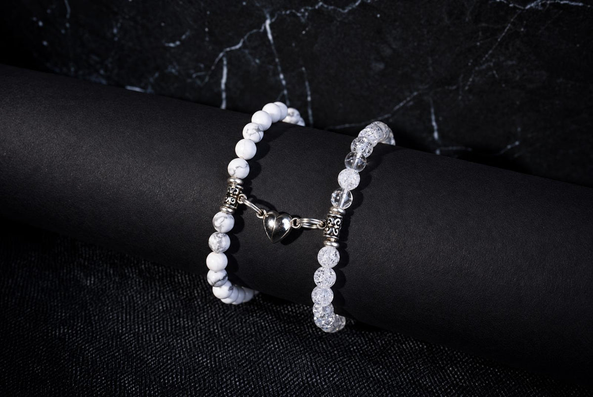 Two bracelets with white veined beads and clear textured beads, ornate silver spacers and linked heart charms against a dark background.