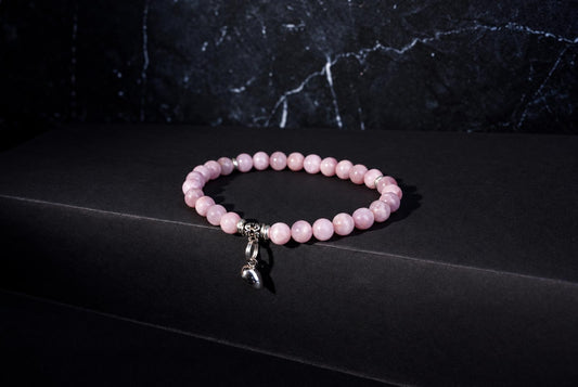 Kunzite bracelet with pale pink round beads, ornate silver spacers and a hanging heart charm against a dark background.